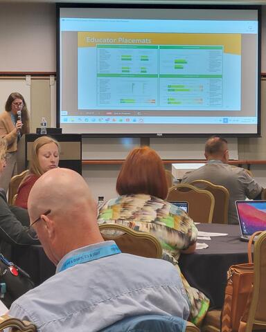 A presenter with a slide showing data to a group of adult educators