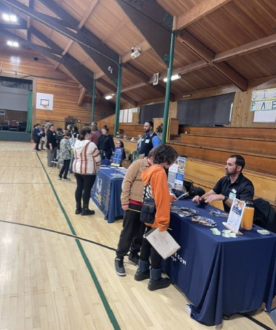 Several students engaging in front of several booths located inside a school gym